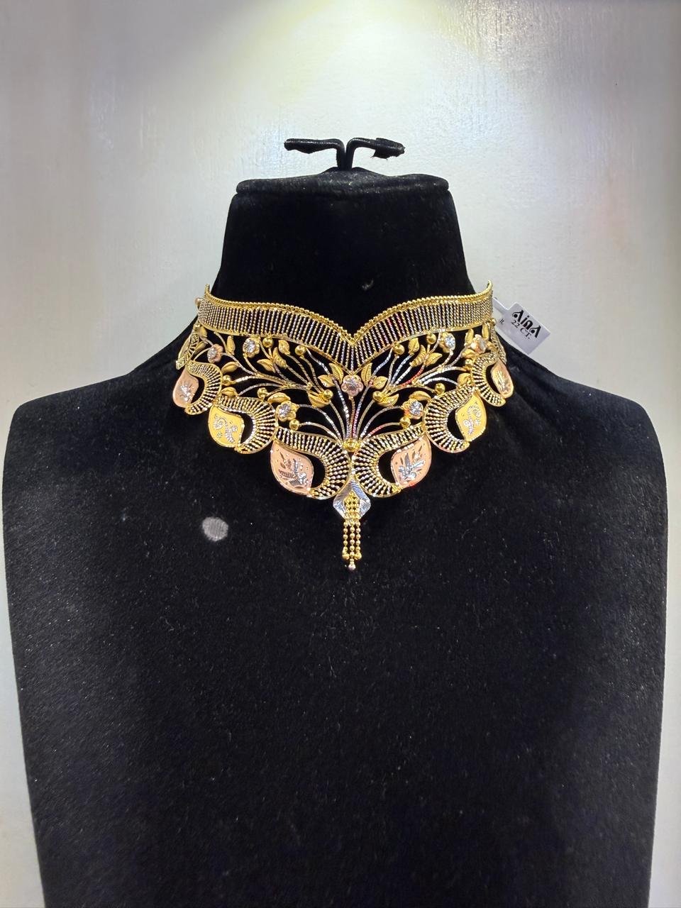 A gold bridal choker with a peacock motif, shown with its Aina purity tag
