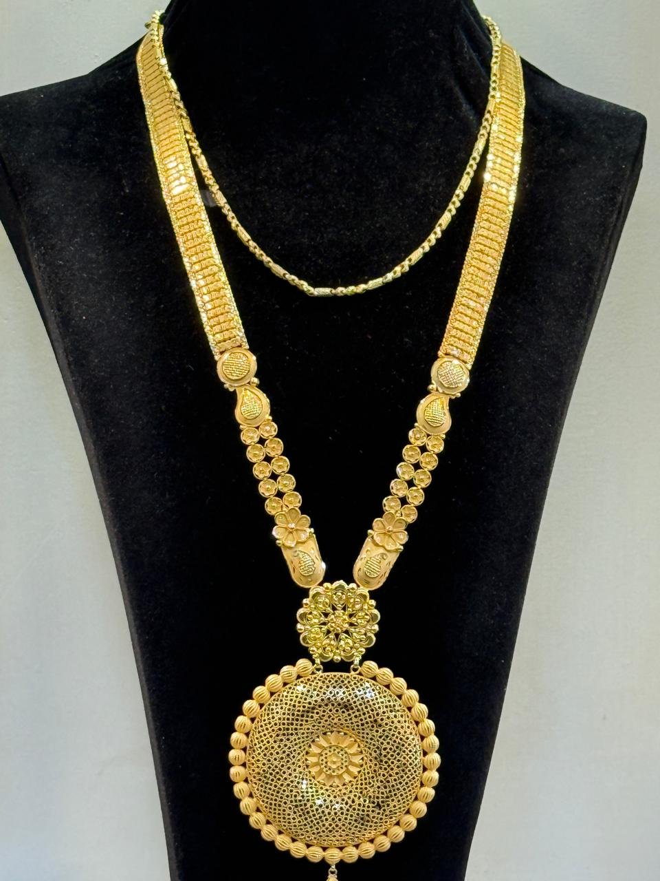 A long gold haram necklace with a round medallion pendant