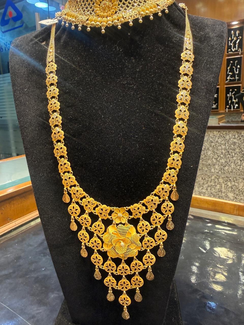 A long tri-tone gold necklace with a floral pendant and tassel drops