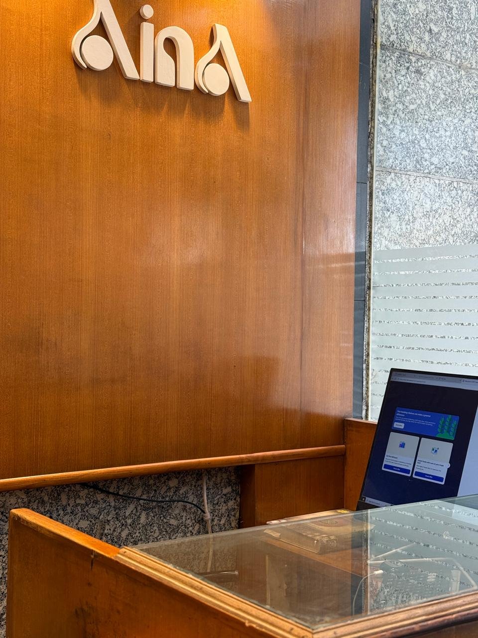 The Aina Gold wordmark, mounted above the reception counter in the showroom